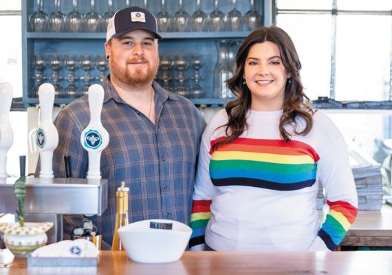 Owners Taylor Benson and Mackenzie Smith standing behind a tasting room bar, smiling.