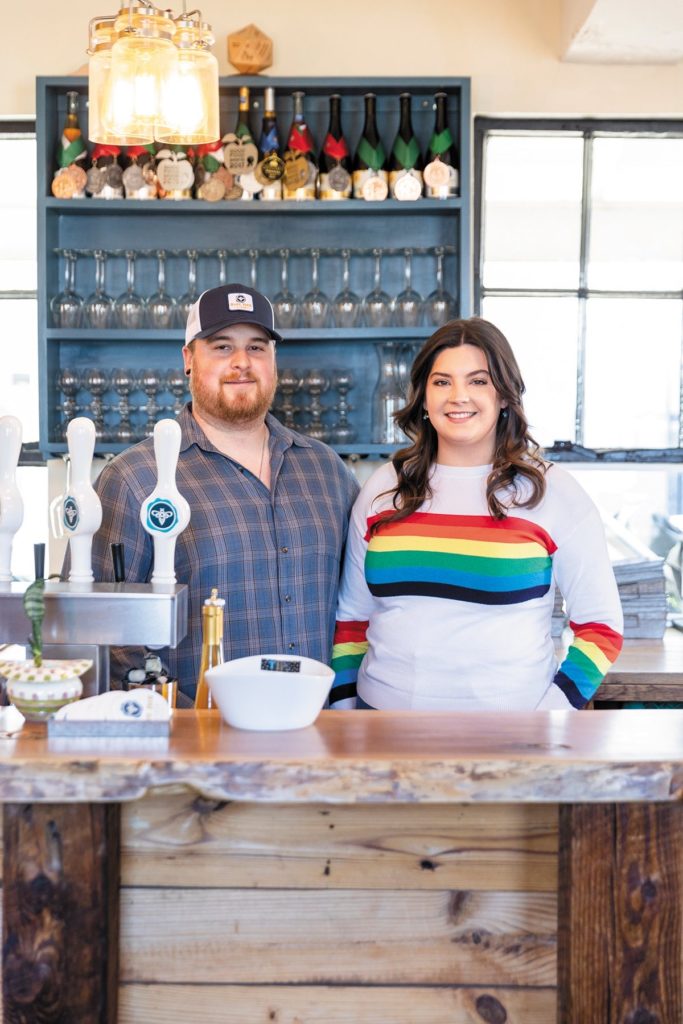 Owners Taylor Benson and Mackenzie Smith standing behind a tasting room bar, smiling.